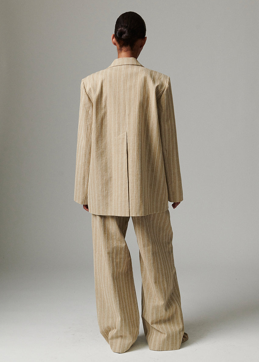 Person wearing a beige pinstripe suit against a plain background