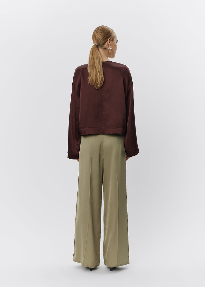 Person wearing a brown sweater and green pants on a white background