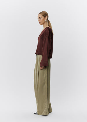 Woman wearing a brown top and green pants on a white background