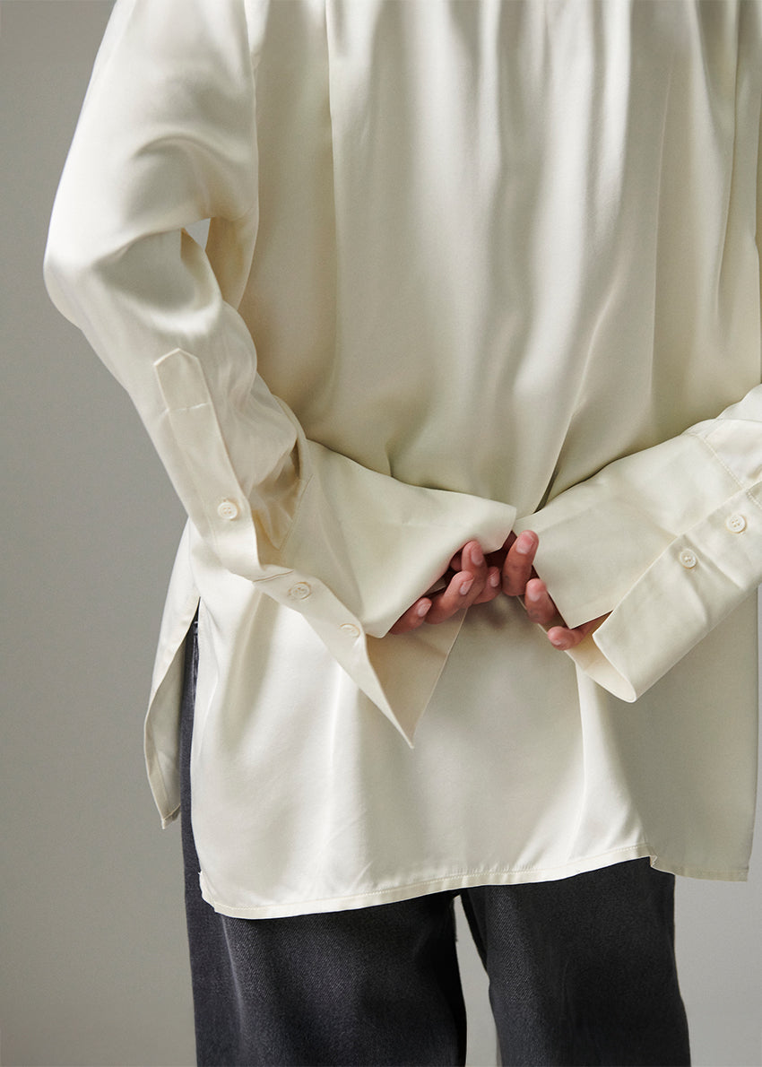 Person wearing a loose-fitting cream-colored shirt with rolled-up sleeves against a neutral background