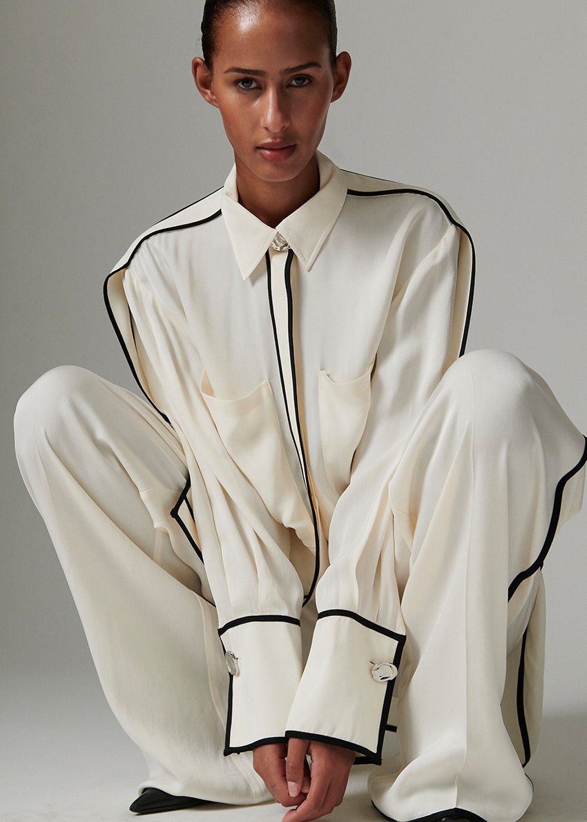 Person wearing a white outfit with black trim sitting on a gray background