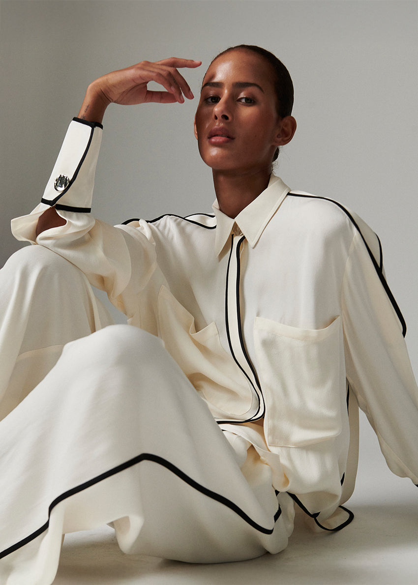 Person wearing a white outfit with black trim sitting against a neutral background