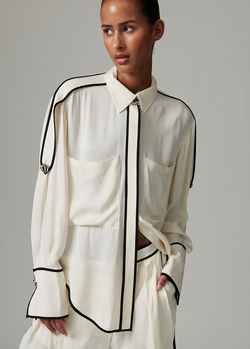 This fluid, button-up top features contrast piping, epaulets at the shoulders, and a dipped hem. There are two pockets at the chest.