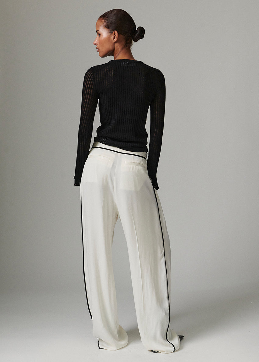 Woman wearing a black long-sleeve top and white pants with black stripes on a gray background