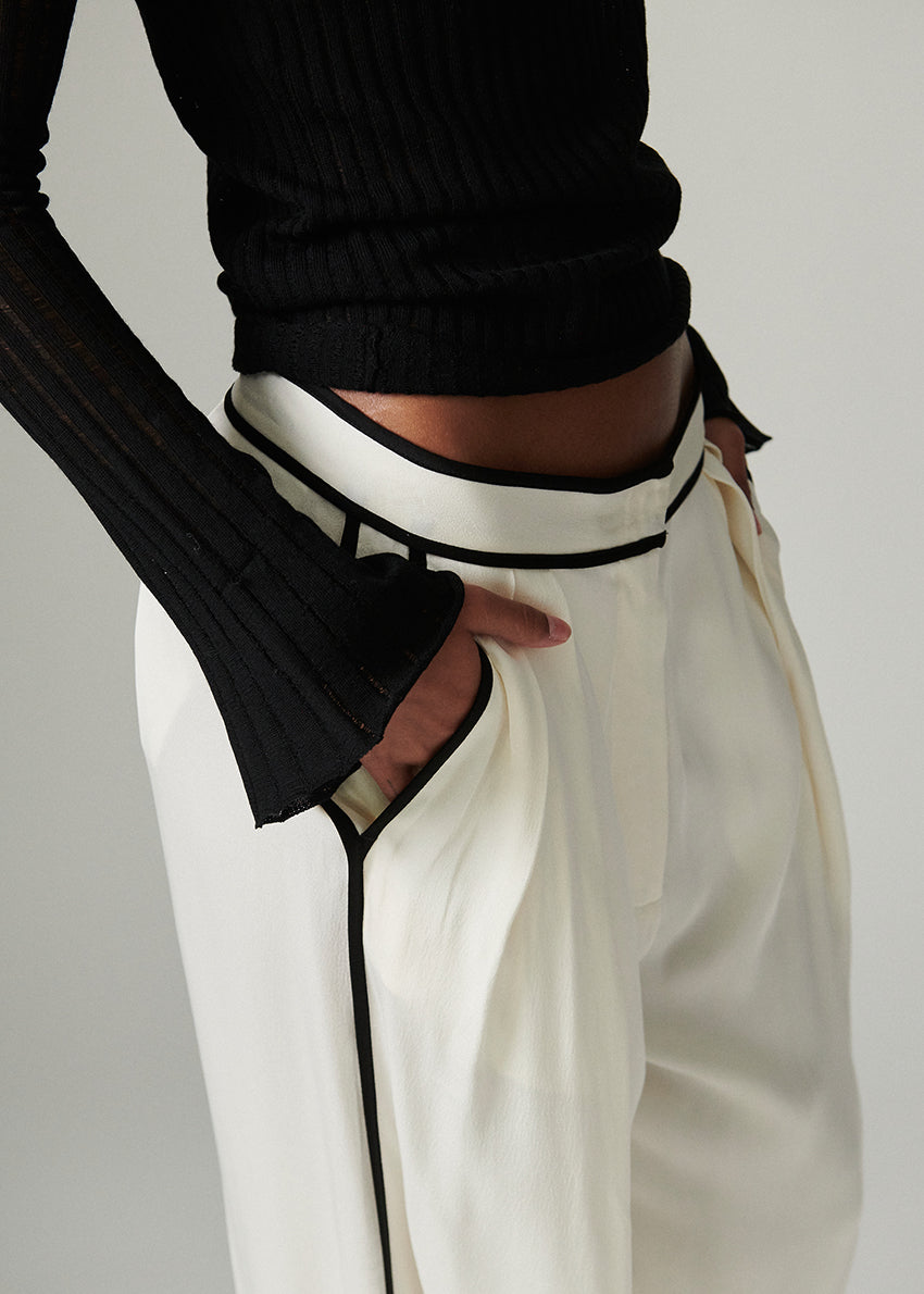 Person wearing a black sweater and white pants with black trim on a plain background