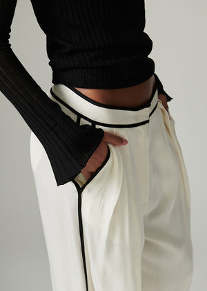 Person wearing a black sweater and white pants with black trim on a plain background