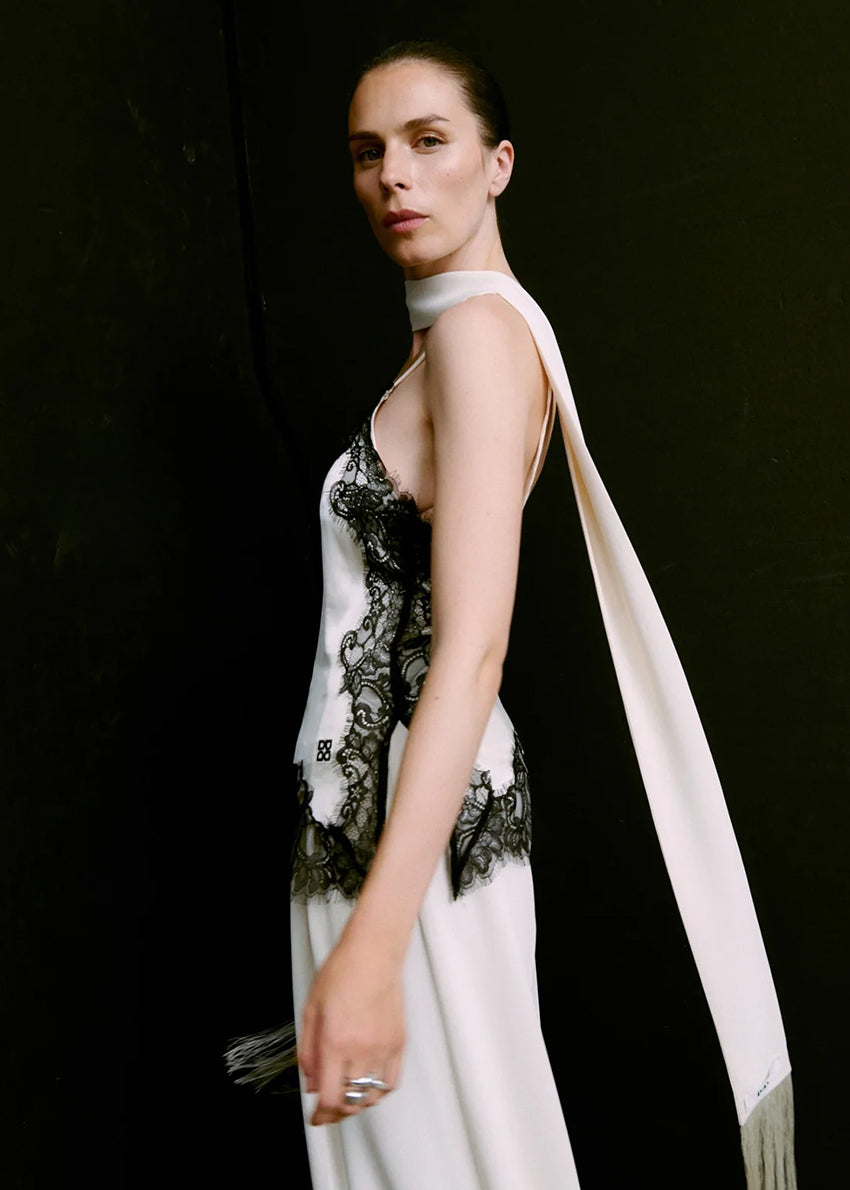 Woman wearing a white top with black lace details against a dark background