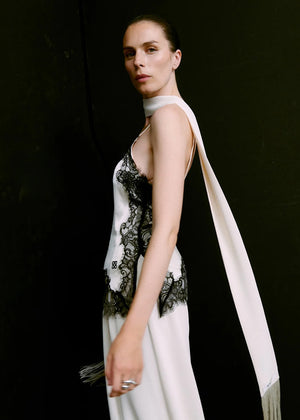 Woman wearing a white top with black lace details against a dark background