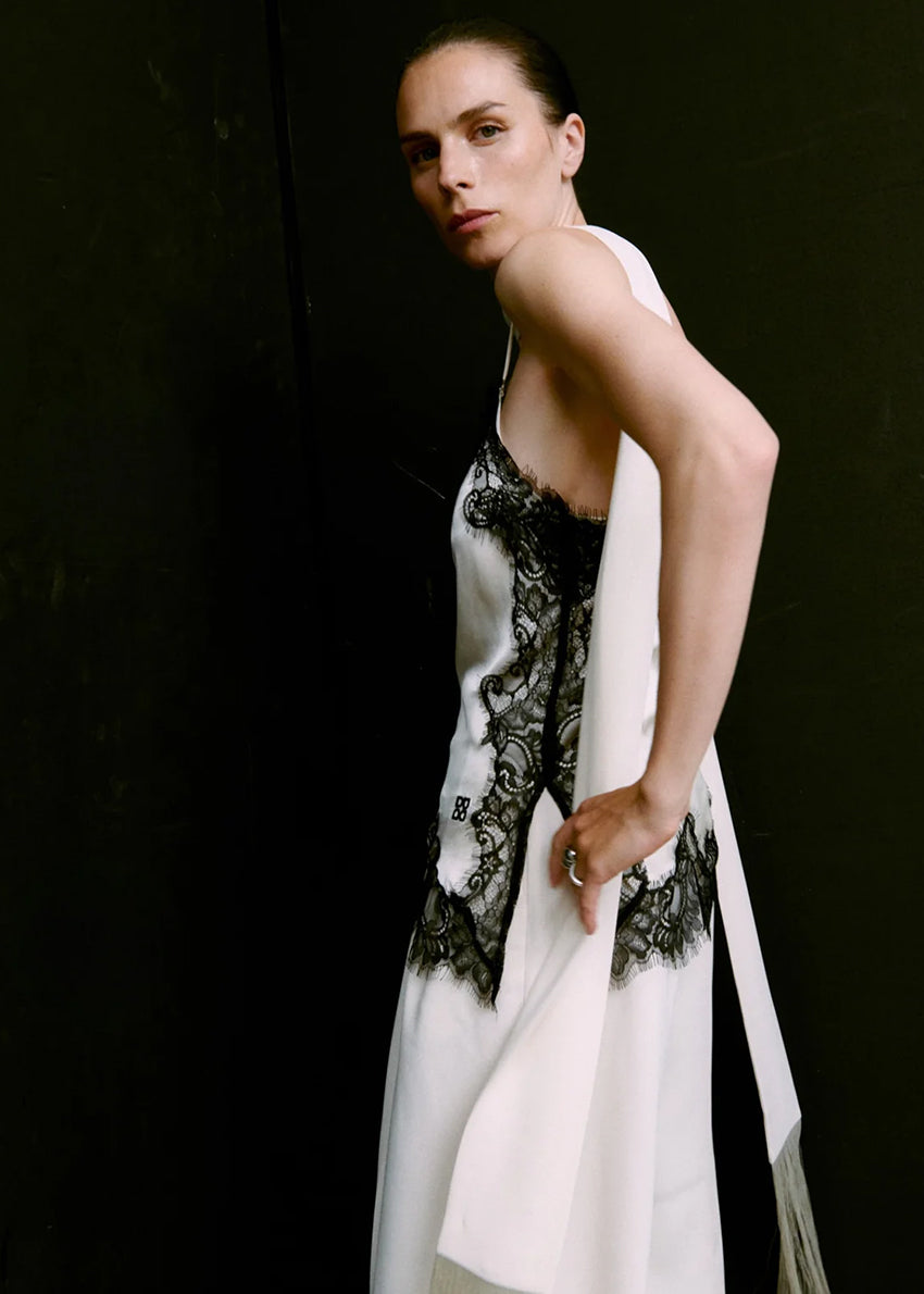 Woman wearing a white top with black lace details against a dark background