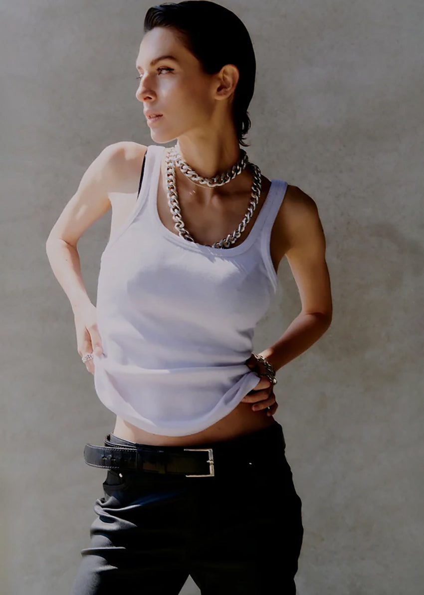 Person wearing a white tank top and black pants with a neutral background