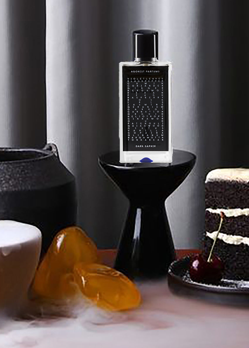 Perfume bottle on a small black table with a cake and decorative elements in the background