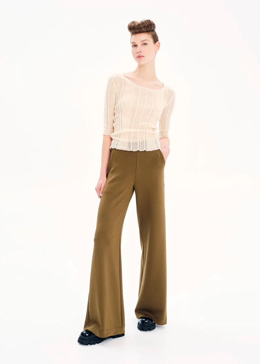 A woman modeling a beige knitted top with rib pattern and 3/4 sleeves, paired with green trousers.