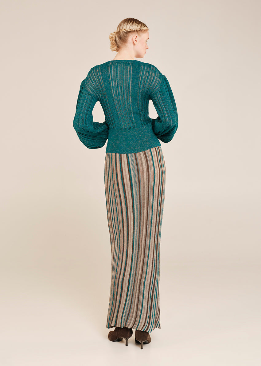 Woman wearing a teal sweater and striped skirt on a beige background