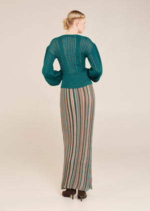 Woman wearing a teal sweater and striped skirt on a beige background