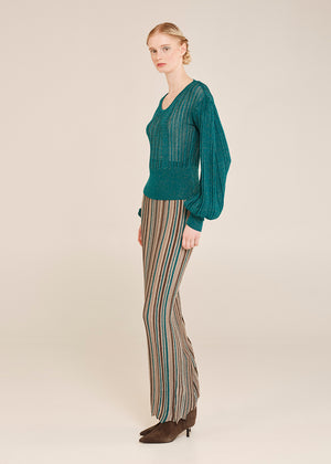 Woman wearing a teal sweater and striped pants on a beige background