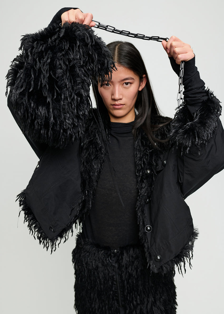 Person wearing a black fur-trimmed coat against a plain background