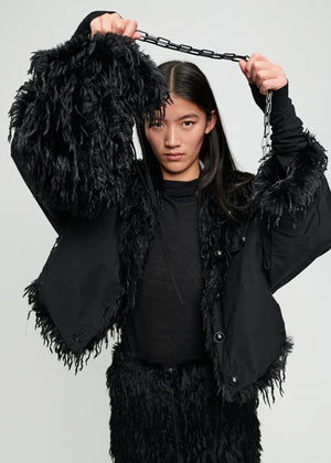Person wearing a black fur-trimmed coat against a plain background