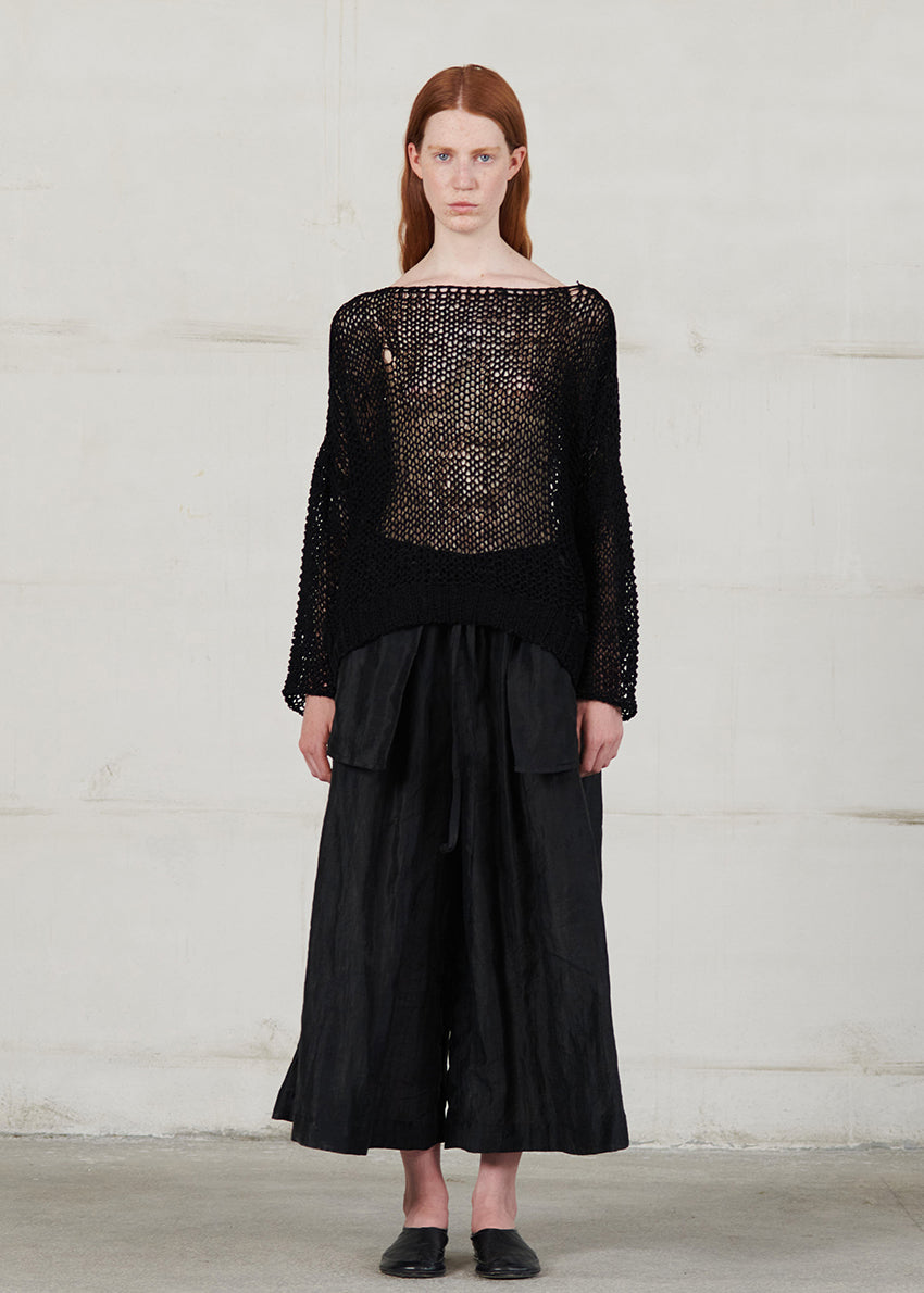 Model wearing a black outfit with a textured top and wide-leg pants against a plain background