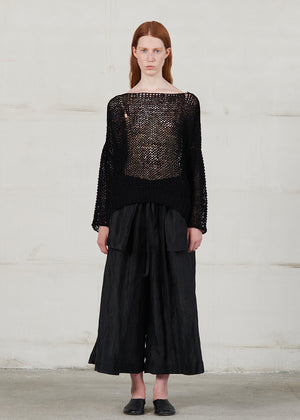 Model wearing a black outfit with a textured top and wide-leg pants against a plain background