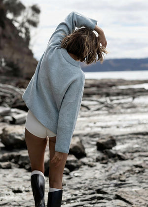 Person wearing a light blue sweater and white shorts on a rocky beach.