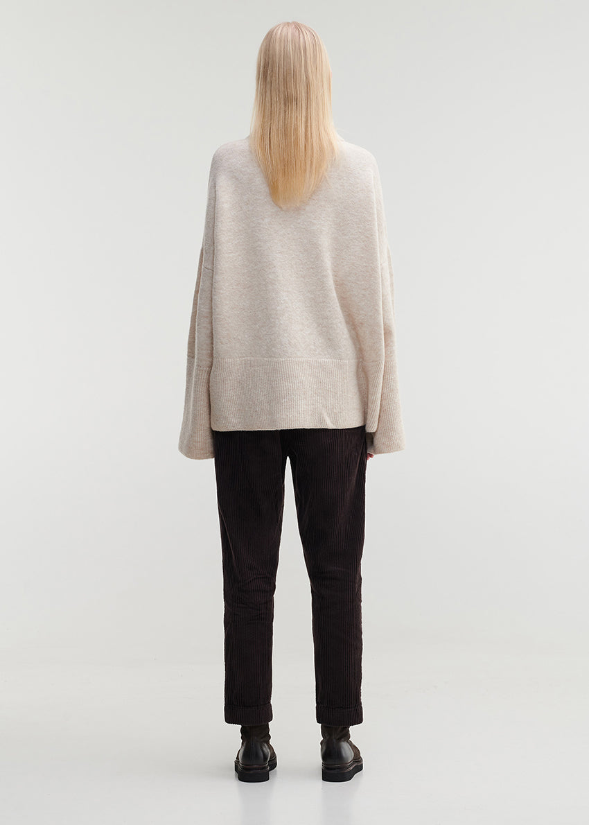 Person wearing a beige sweater and dark pants on a white background