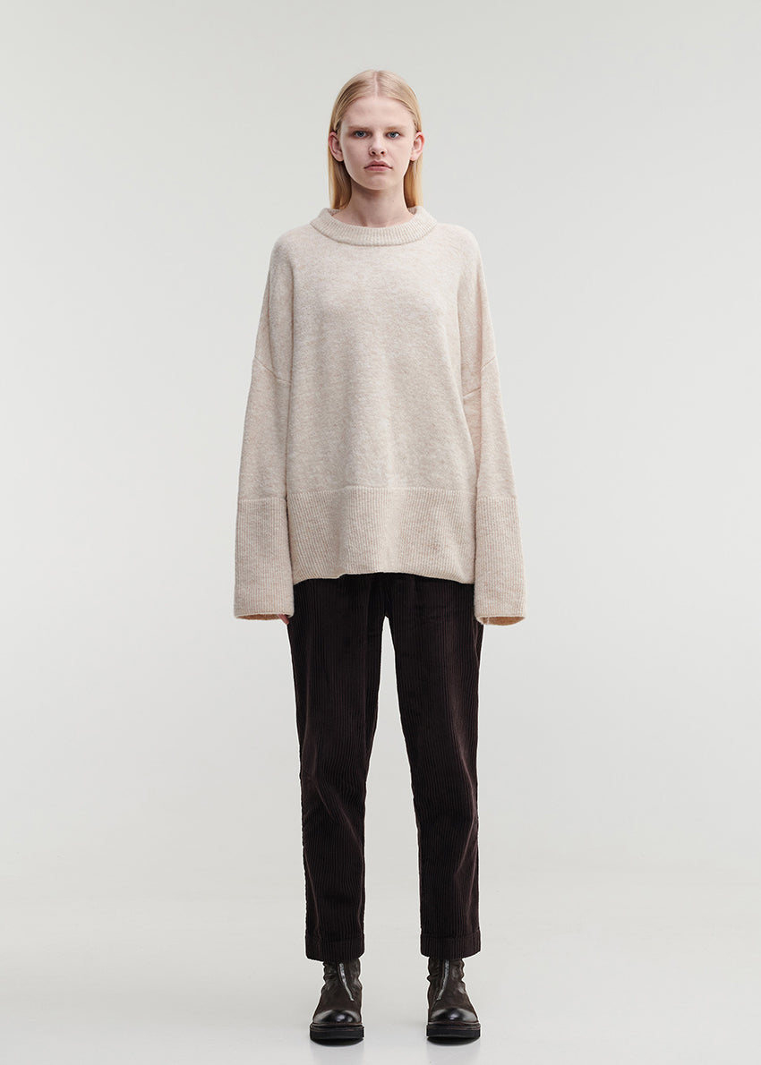Person wearing a beige sweater and black pants on a white background