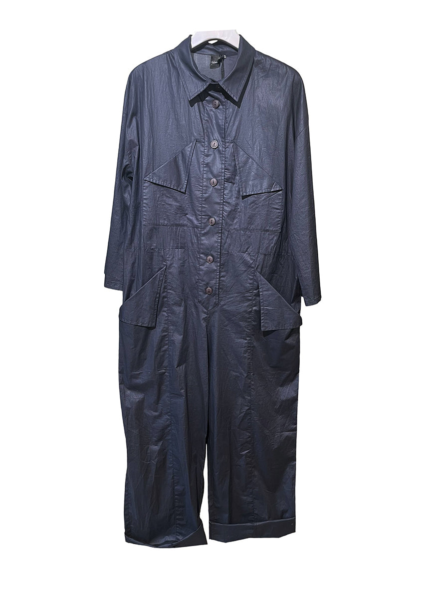 Woman wearing a jumpsuit standing against a dark wall.