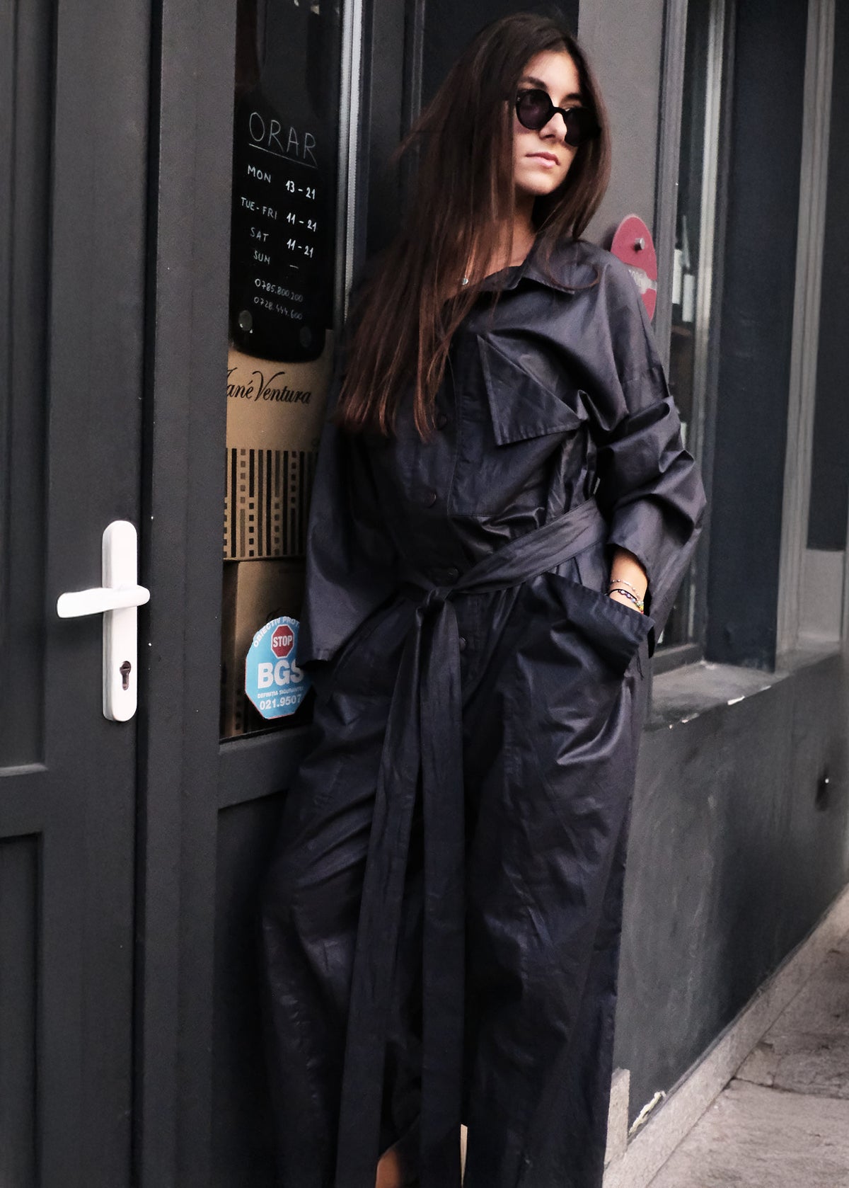 Woman in a jumpsuit standing next to a door with posters on it.