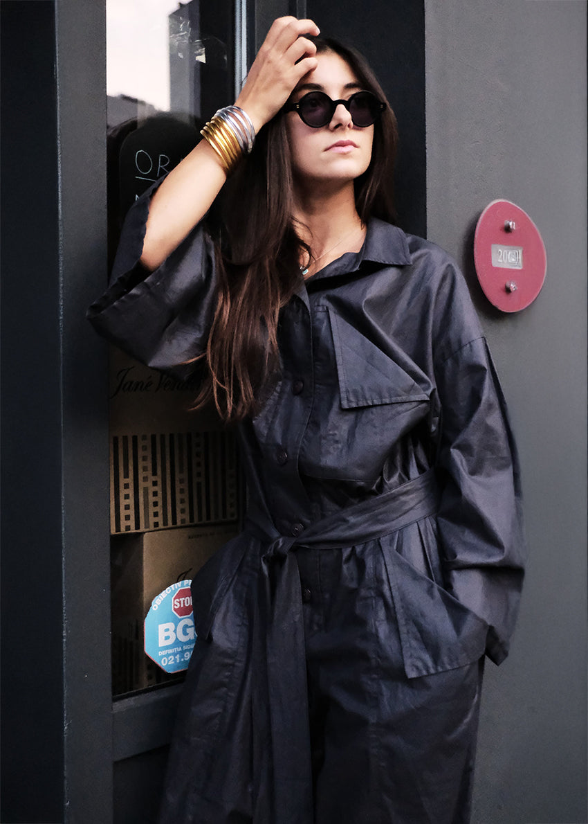 Woman in a black jumpsuit standing next to a payphone with a red button.