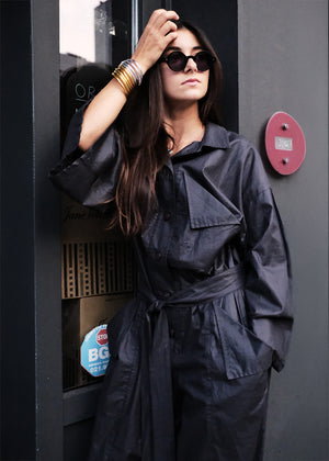 Woman in a black jumpsuit standing next to a payphone with a red button.