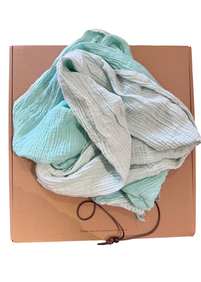 Stack of light-colored fabric on a cardboard box with a brown strap.