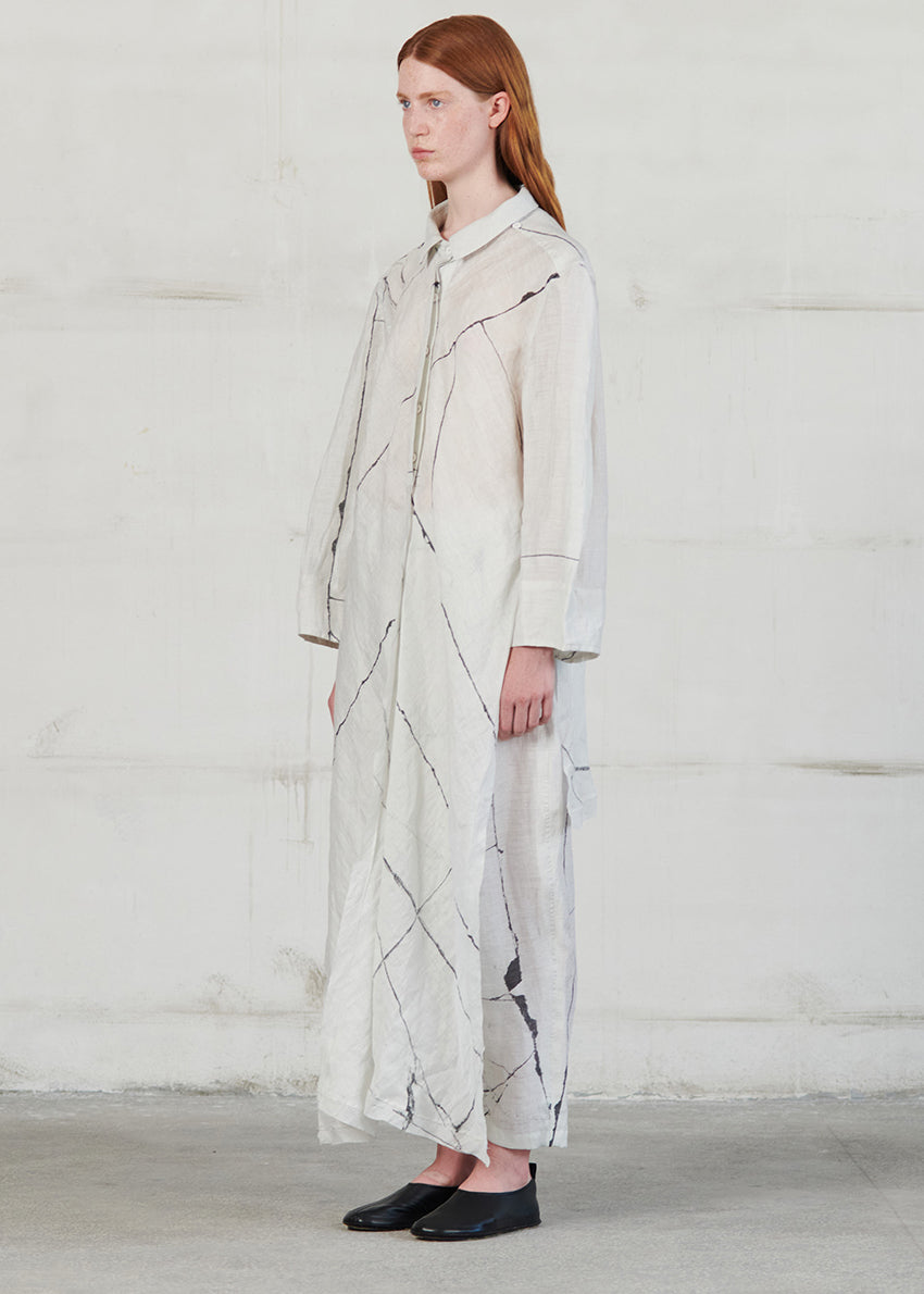 Woman wearing a long, light-colored shirt with abstract patterns against a plain background
