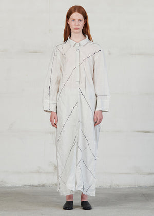 Woman wearing a long, light-colored shirt with geometric patterns against a plain background