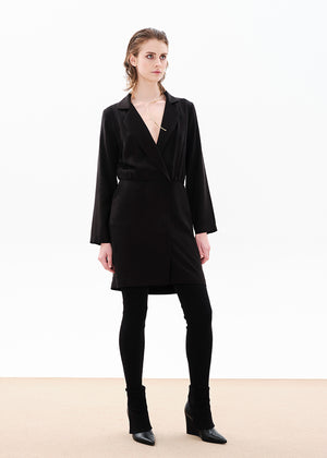A female model wearing a black draped blazer dress with a V-neck collar, long sleeves, and a two-way zipper front.