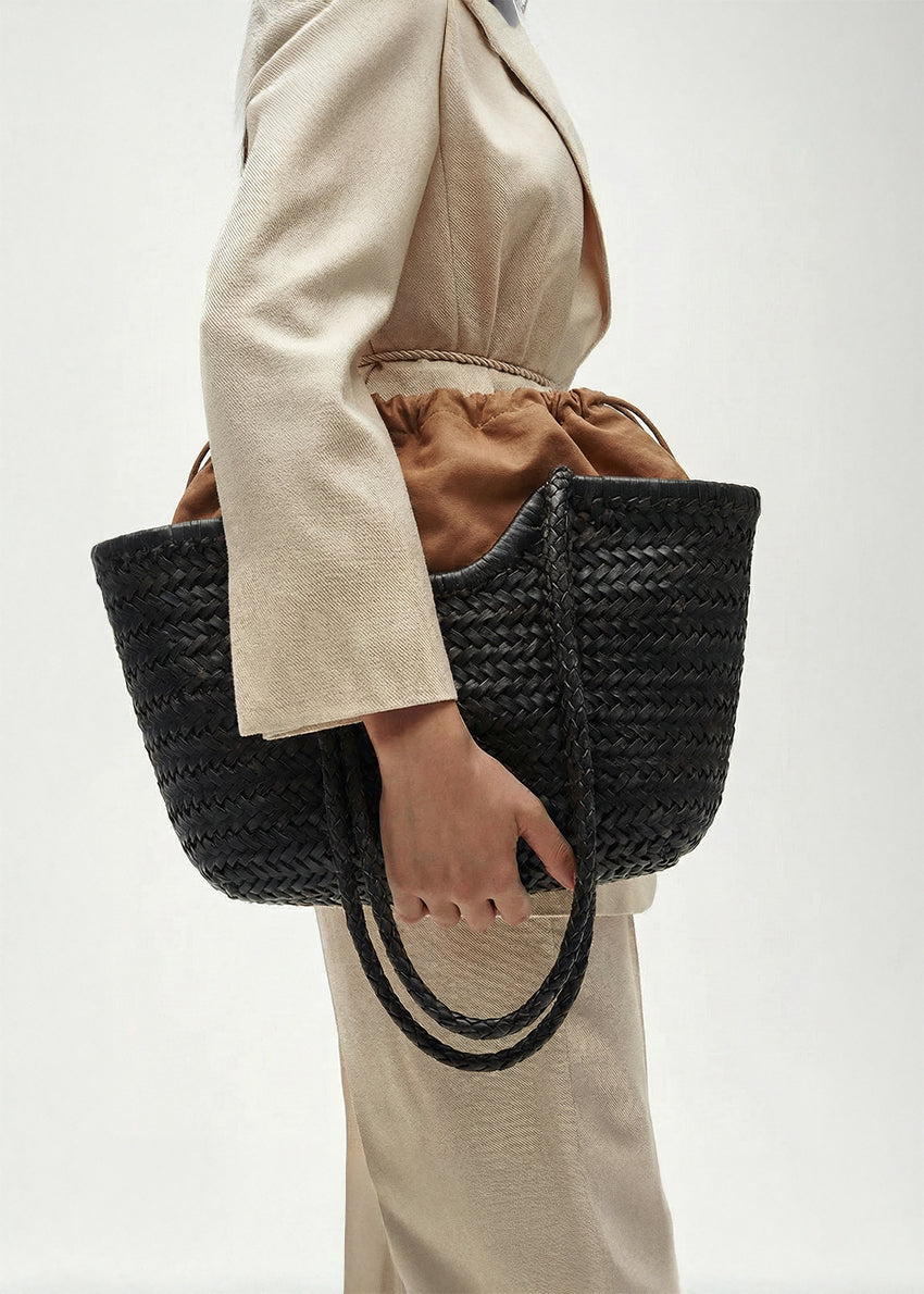 Person holding a black woven handbag against a neutral background