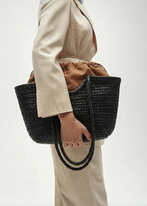 Person holding a black woven handbag against a neutral background
