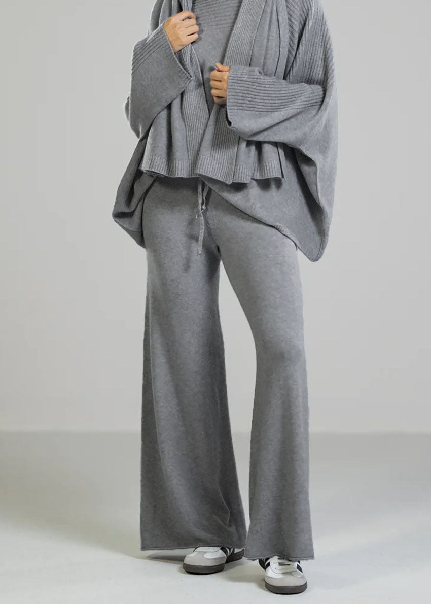 A person sitting on a stool wearing long wide beige pants with an elastic drawstring, paired with a striped shirt and a headscarf.