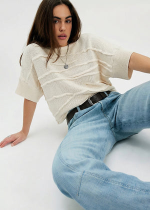 Woman wearing a cream sweater and light blue jeans on a white background