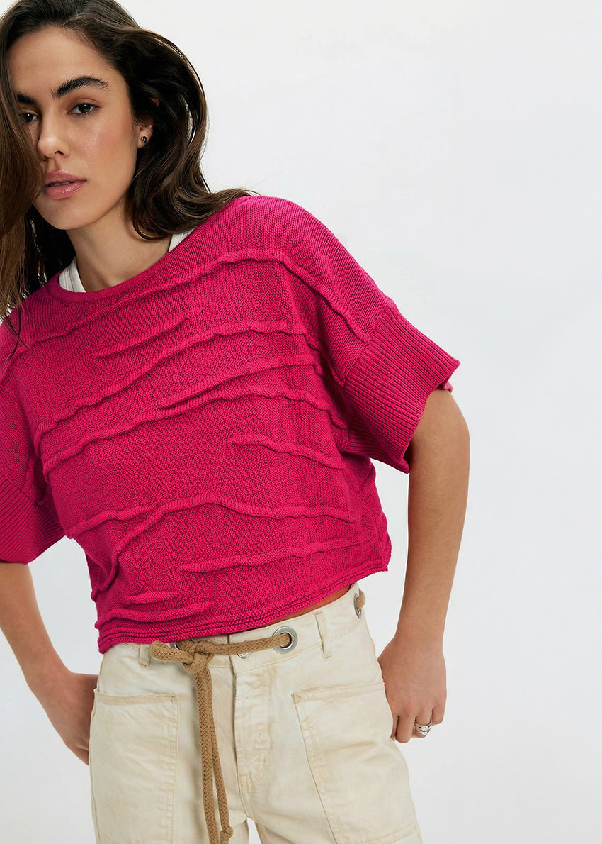 Woman wearing a bright pink sweater and beige pants on a white background