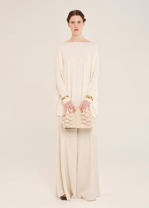Woman wearing a cream-colored oversized top with a matching handbag on a plain background