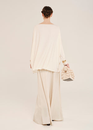 Person wearing a cream outfit with a matching handbag on a white background