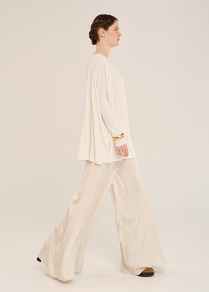 Woman wearing a cream-colored outfit on a plain background