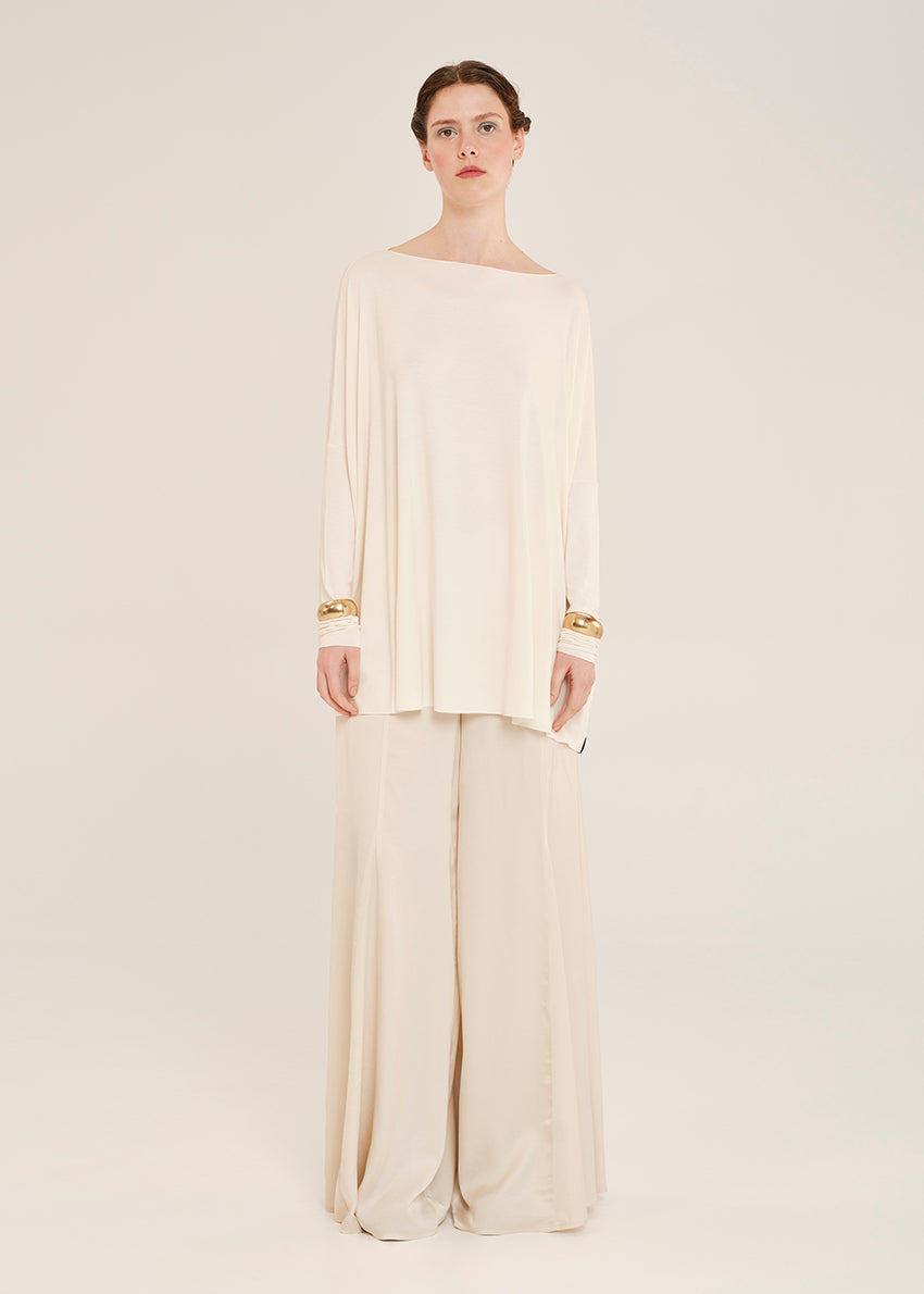 Woman wearing a cream-colored outfit with wide-leg pants on a light background