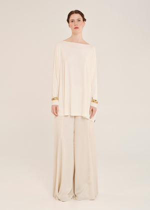 Woman wearing a cream-colored outfit with wide-leg pants on a light background