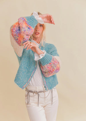 Woman wearing a colorful knitted cardigan with a plain background