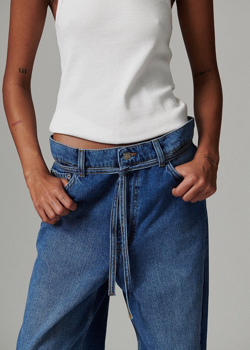 Person wearing a white top and blue jeans with a tie-waist design on a gray background