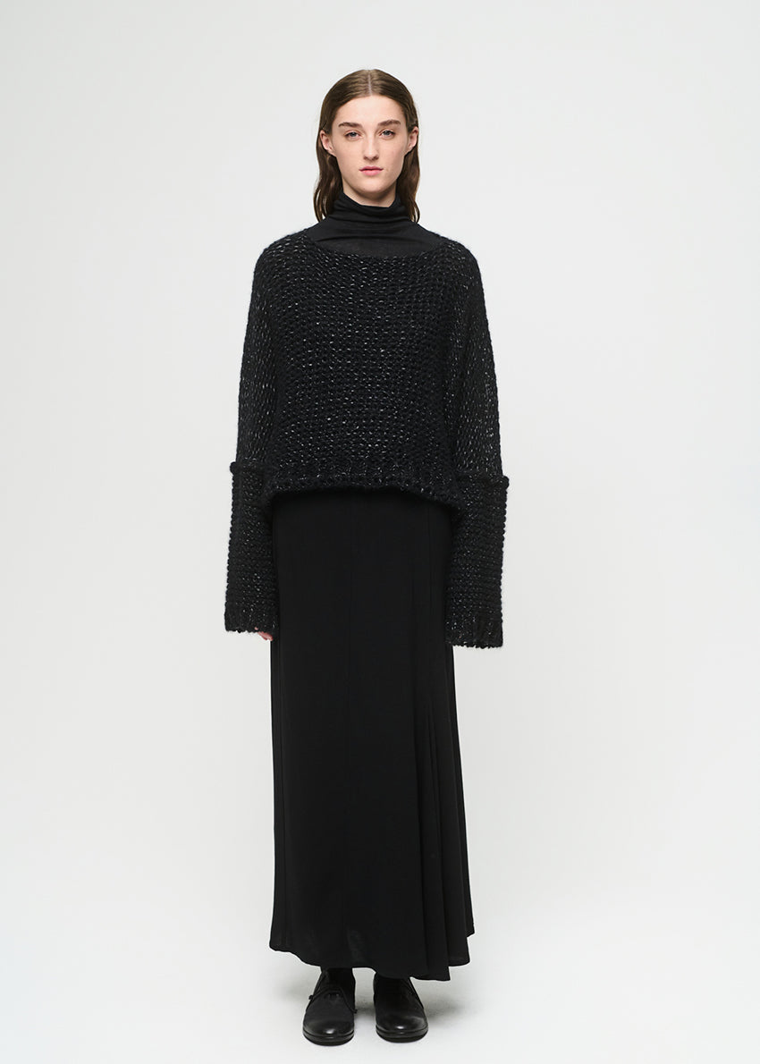 Person wearing a black knit sweater and black skirt on a white background