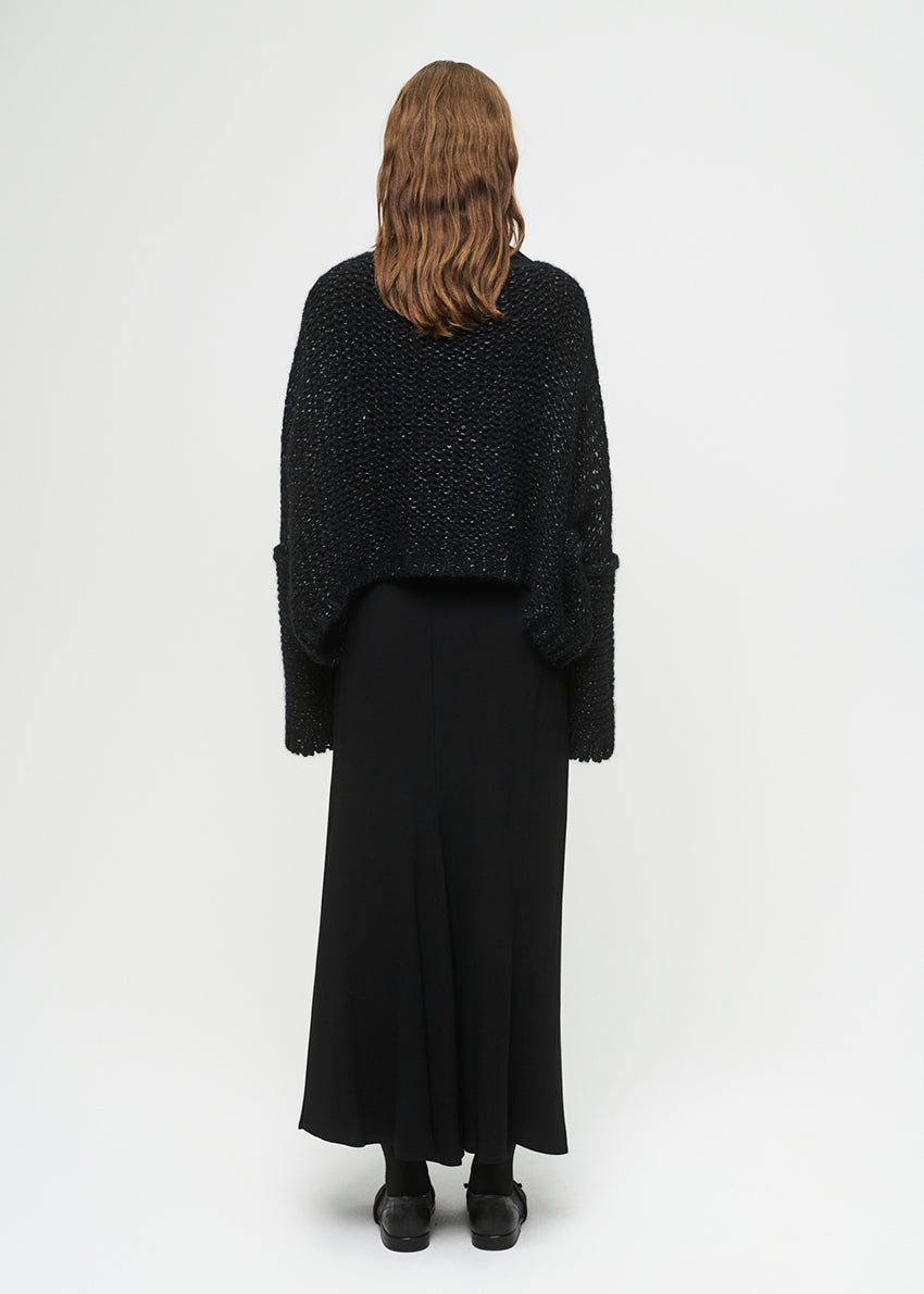 Person wearing a black textured sweater and long black skirt on a white background