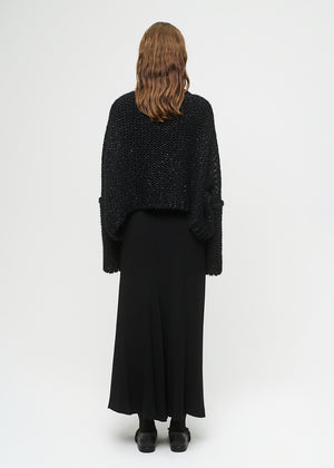 Person wearing a black textured sweater and long black skirt on a white background