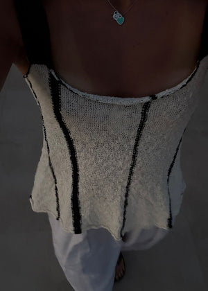 Person wearing a white knitted top with black stripes and white pants on a dark background